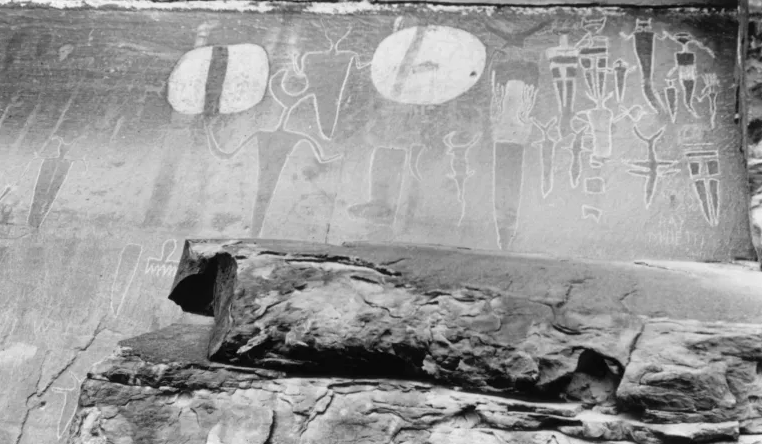 A black and white photo of pictographs at Courthouse Wash; the figures depicted are humanoid and appear to be holding shields.