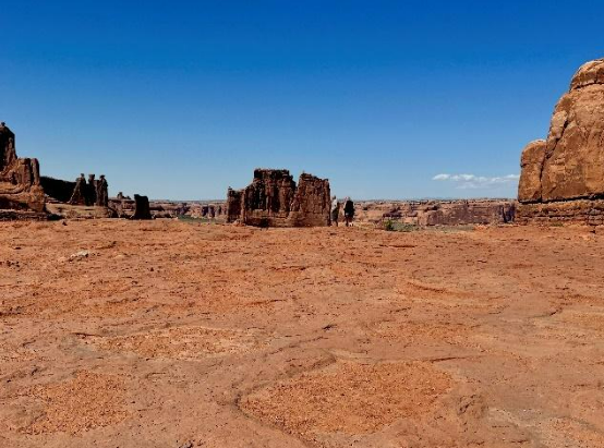 The view shows a flat sandstone expanse leading to a viewpoint of sandstone towers