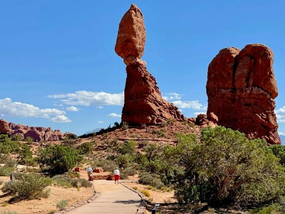 A photo of Balanced Rock, an enormous boulder that appears to be balanced on the tip of a sandstone pile. The frame shows the flat sidewalk that circles the rock.