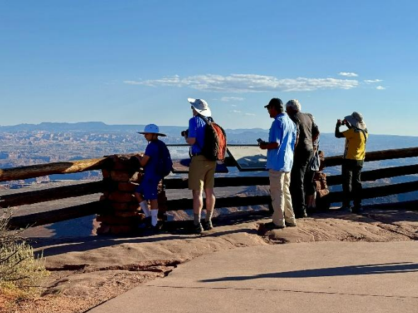 The path to the overlook stops just shy of the fence; the photo shows multiple people standing on a bumpy rock between the path and the fence to look over the edge.