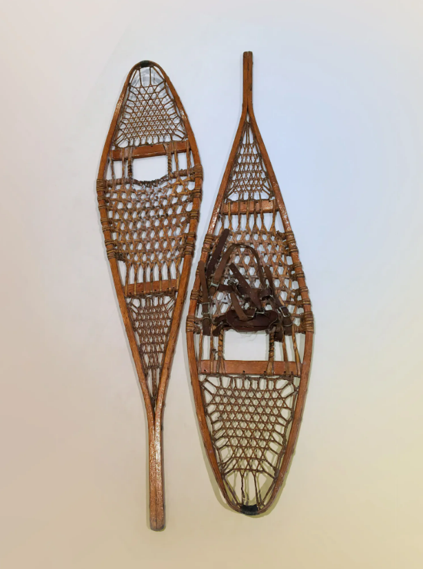 A pair of historic snowshoes against a white background. The snowshoes are made of wood and rawhide lacing.