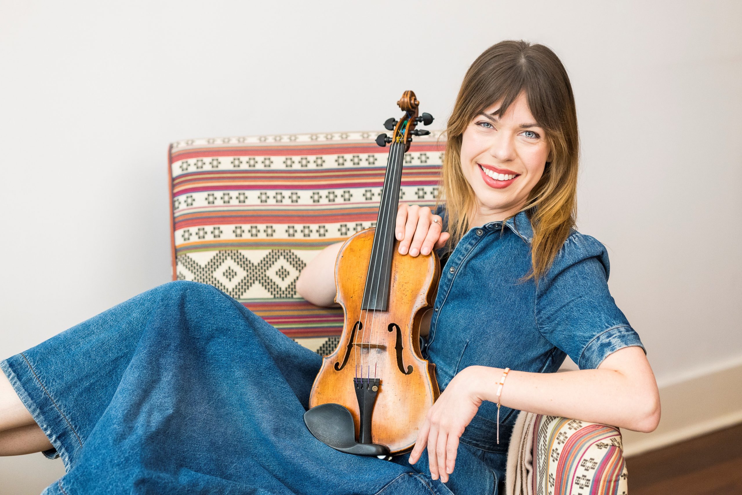 Tessa Lark, a middle-aged brunette woman, lounging in a chair with her violin.