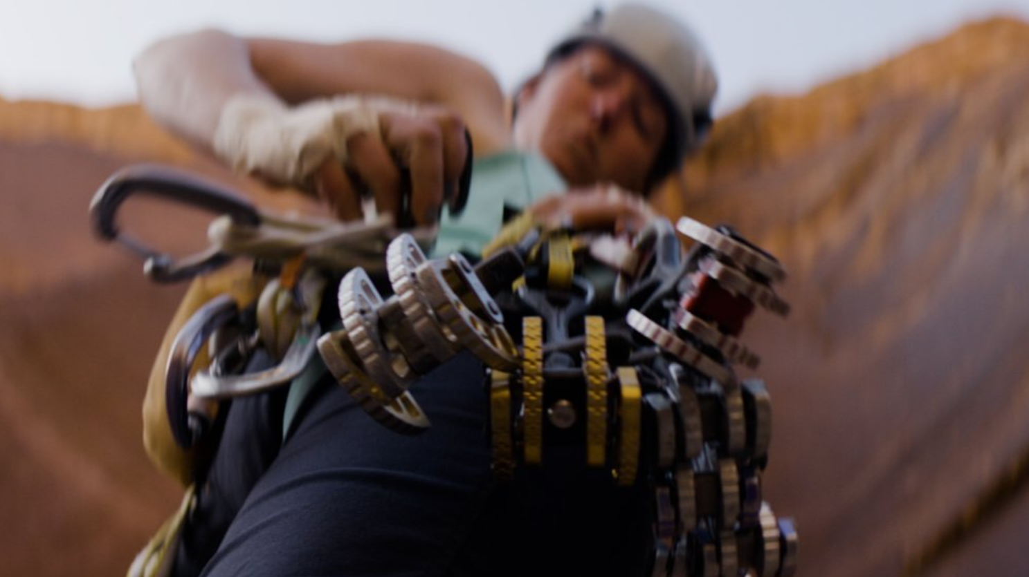 A blurry photo of a person with a trad rack from below their waist, focusing on the gear