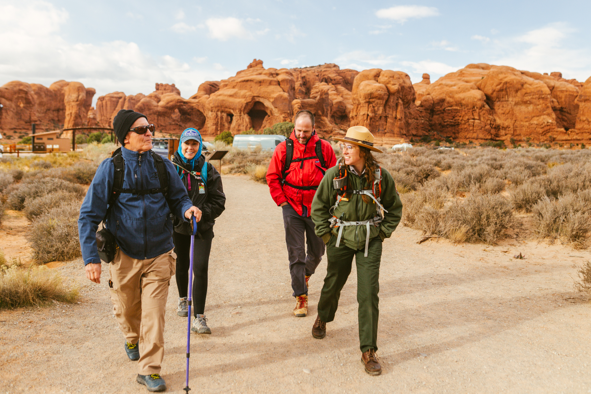 Three people hiking behind a ranger in Arches National Park, they're all chatting